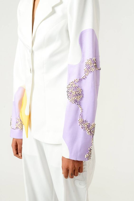 Ivory suit with hints of lilac and yellow is such a pleasant sight. This two-piece suit look has adorable details that stand out so subtly. It’s a must have for an elegant, chic and unique look. Shine in this ivory and lilac blazer stitched out in poly velvet satin. It features embroidery detail on sleeves, rope detail on yellow panel made out of banana crepe and a front button opening. This out of ordinary pair of ivory trousers stand out due to its interesting PU leather laser cut patch work.