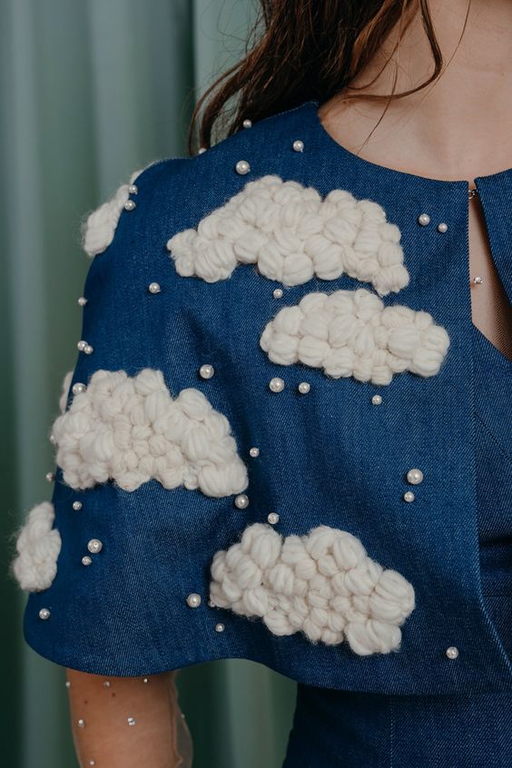 Irresistibly playful mid-arm length cape in deep blue denim with fluffy hand-embroidered yarn clouds, embellished with crystal pearls. Composition: 100 % cotton denim Lining: 100 % silk Details: hand embroidery